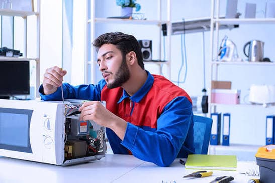 Technician repairing a microwave oven in a service workshop